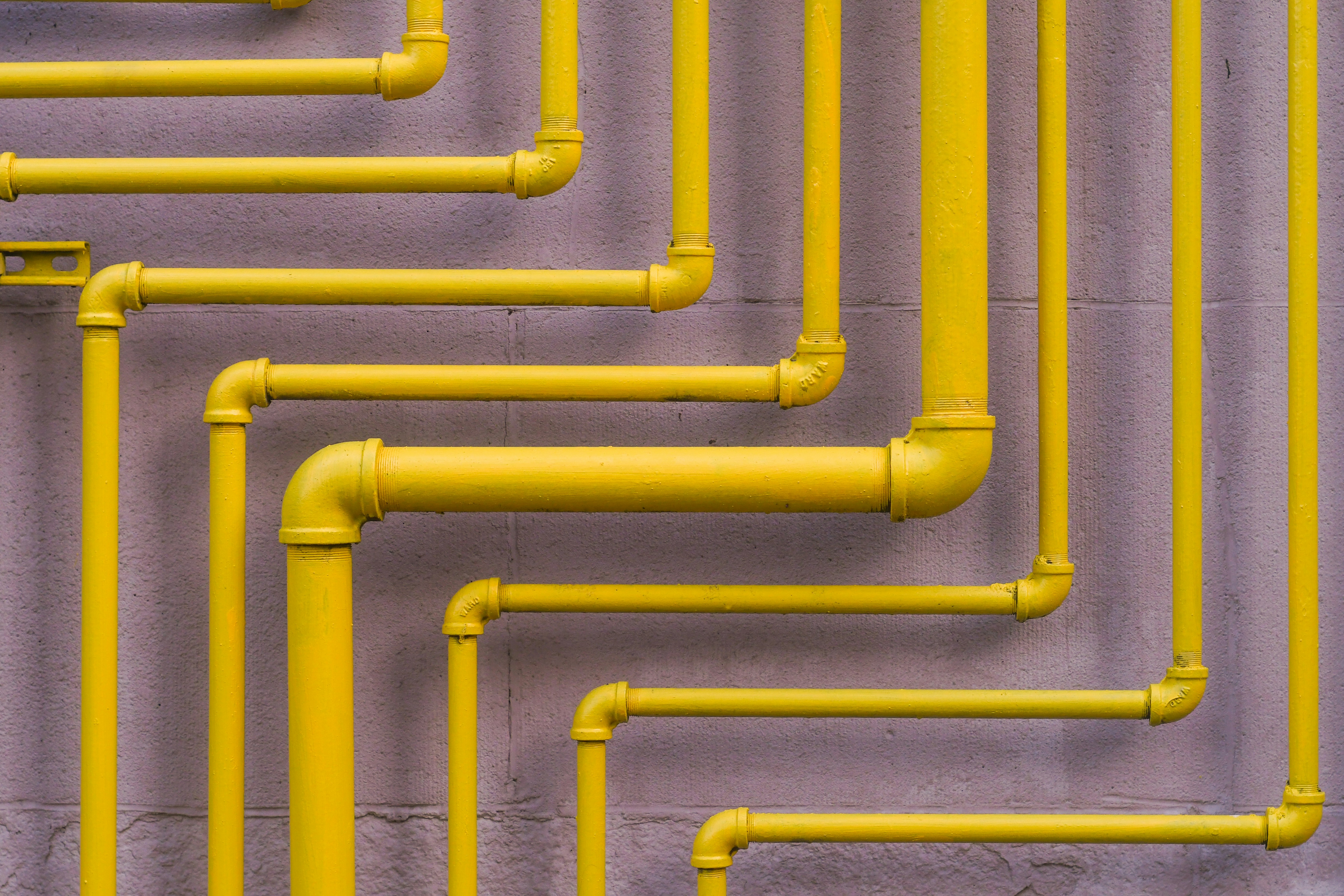 Yellow metal pipes running across a purple wall in a geometric pattern.